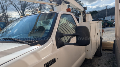 Ford F-550 bucket truck cab with boom lift in service; side mirror, windshield, and VIN plate visible.