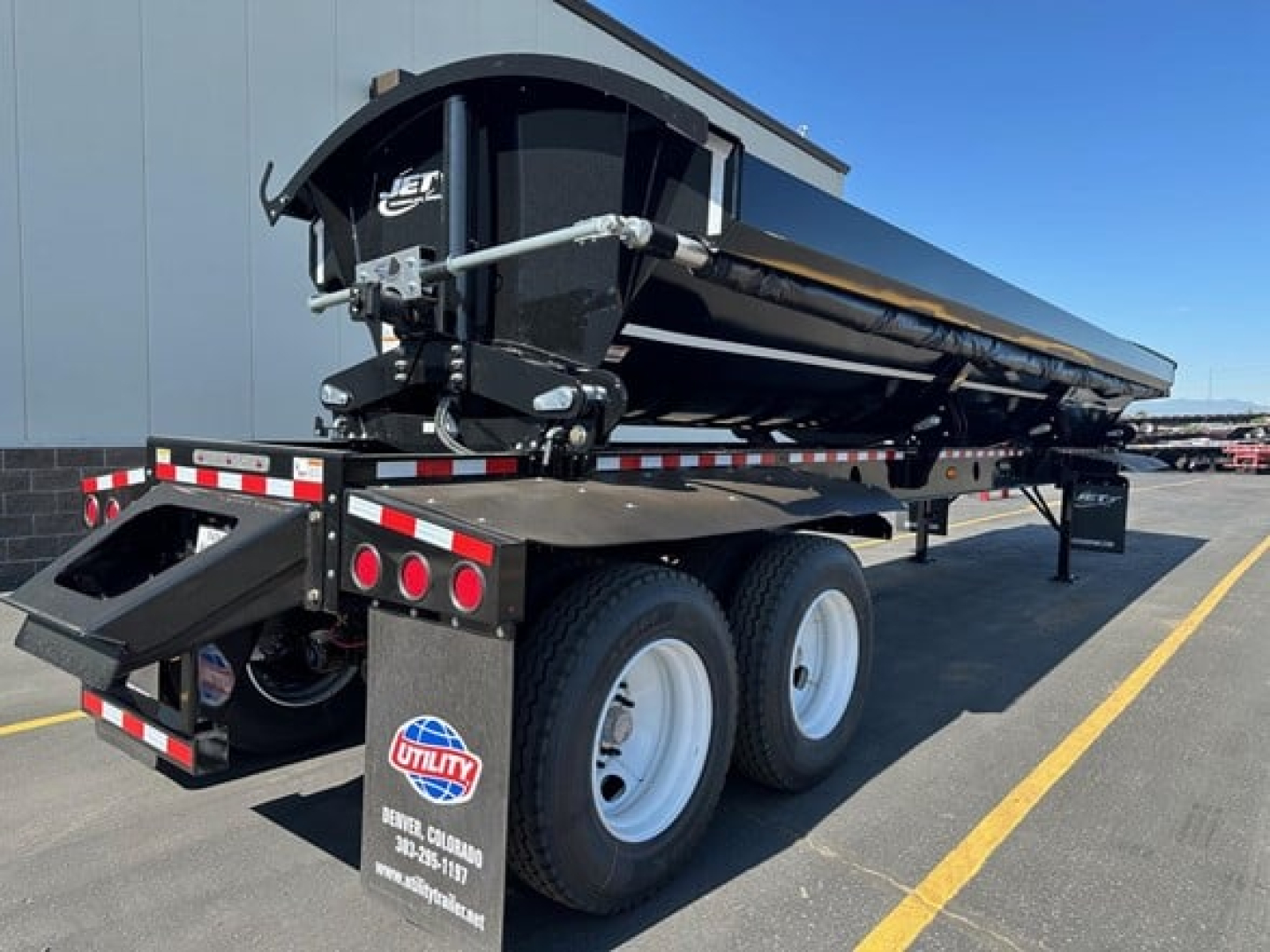 Jet tandem air ride side dump trailer 40' showing hydraulic dumping mechanism and dual axle with white wheels, black frame, and reflective safety markings