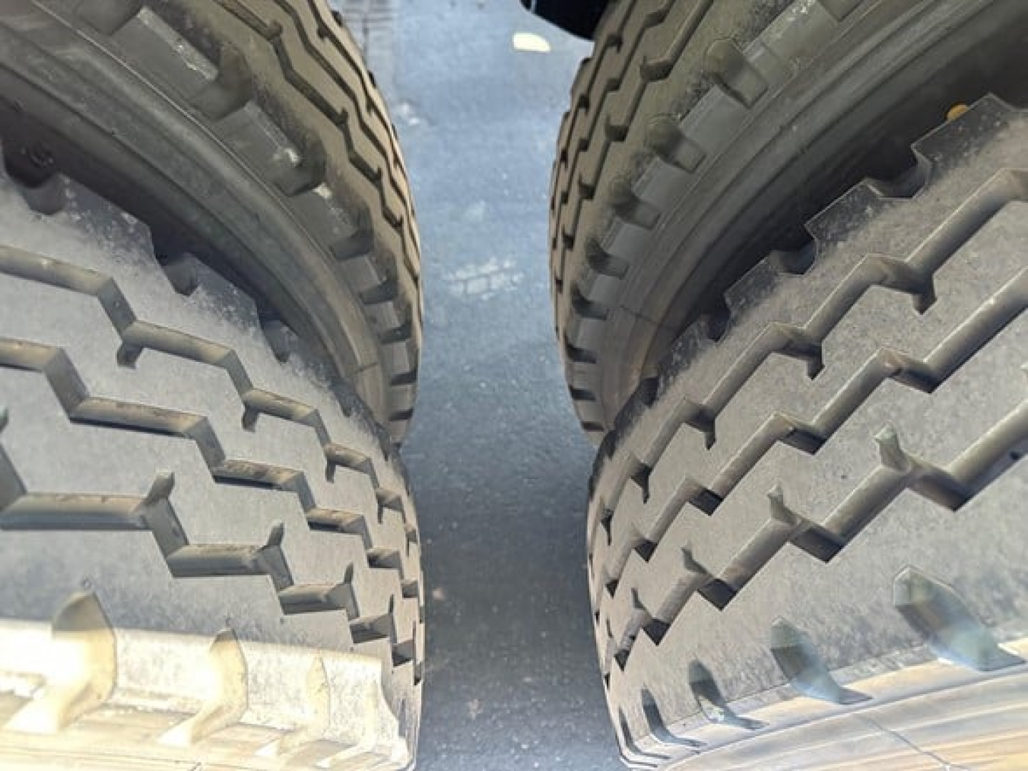 Twin rear tires of a jet tandem air ride side dump trailer showing heavy tread, part of the undercarriage and gap between wheels.