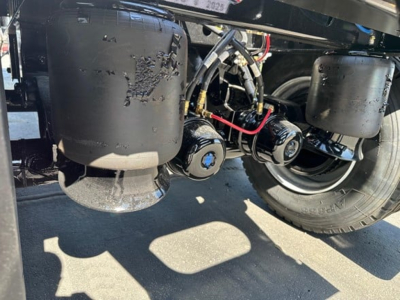 Air ride tandem axle dump trailer undercarriage showing cylindrical air tanks, hoses, axles, and wheel assemblies.