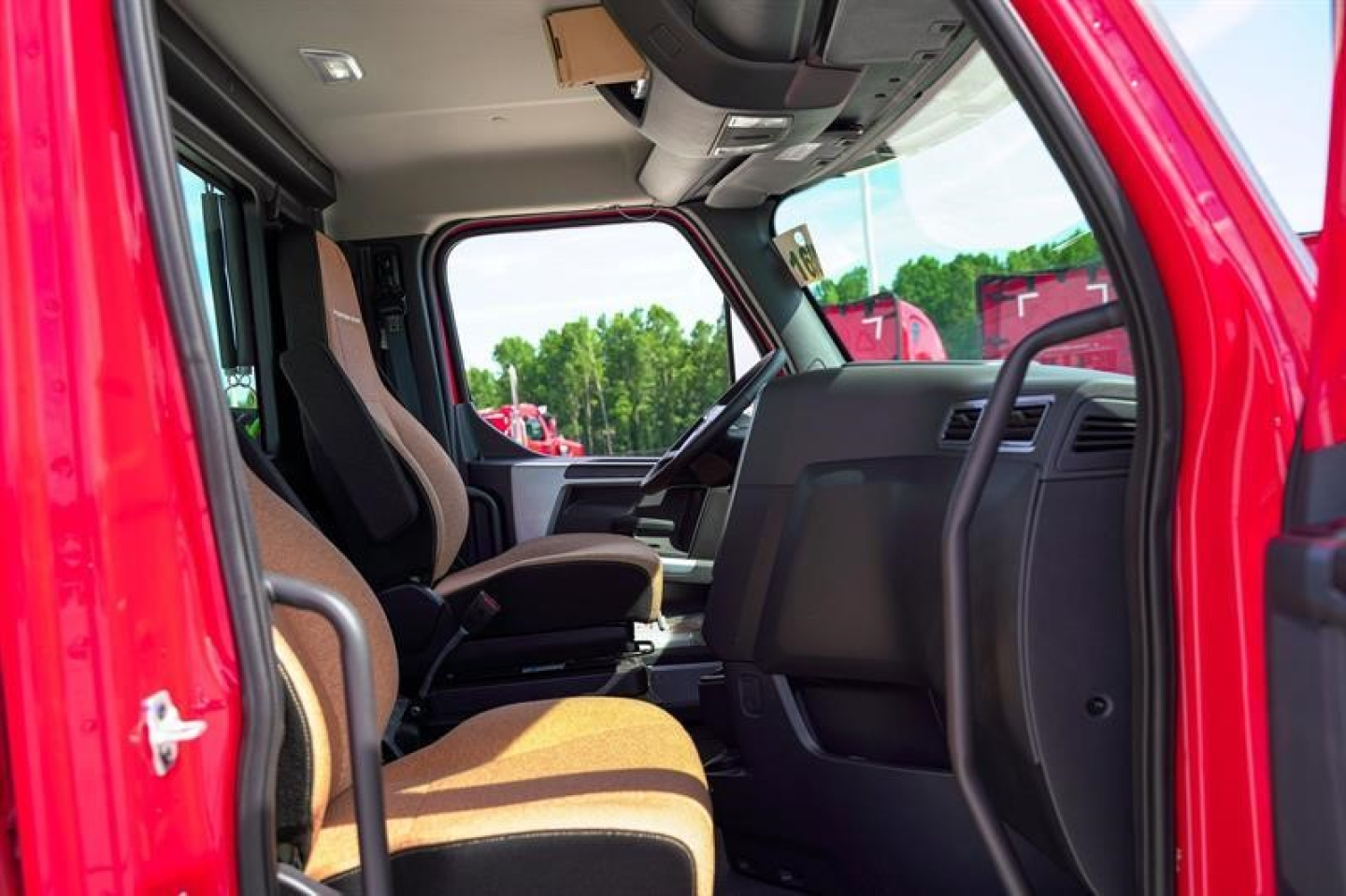 Interior of a new 2027 Western Star 49X day cab showing front seats, dashboard, and open driver door with steering wheel and overhead controls.