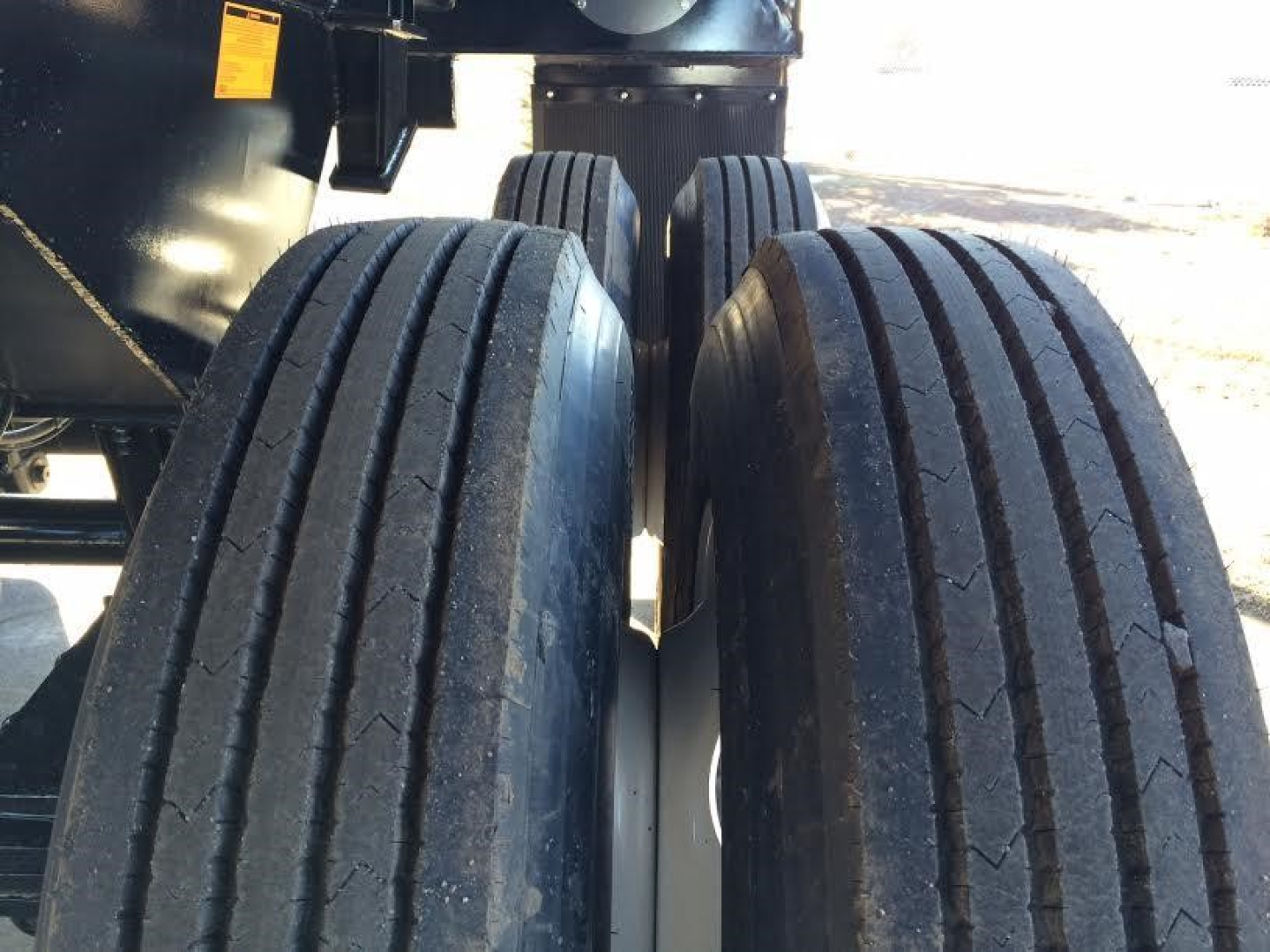Trailer axle area showing dual rear tires of a dump trailer with treaded tires and part of chassis; no visible text on tires.