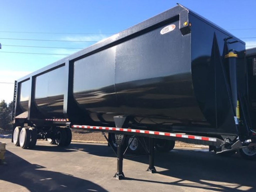 Dump trailer in service showing black rectangular cargo body and tandem axles, reflective tape, landing leg, and gooseneck hitch visible.