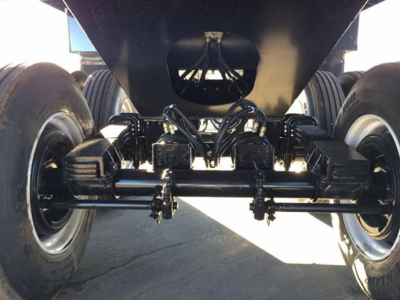 Trailer undercarriage showing dual-axle suspension with leaf springs and multiple hydraulic lines for a dump trailer.