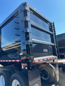 Dump trailer rear view showing heavy-duty steel tailgate with CPS logo, black/blue finish, reflective tape, and dual rear wheels.