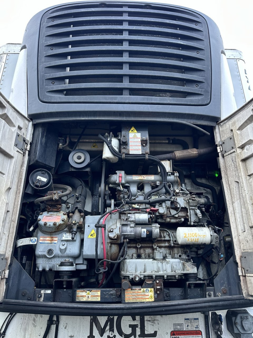 Engine bay of a used 2019 Trail King trailer showing diesel engine with hoses, belts, and warning labels