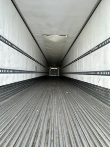 Trailer interior showing long empty cargo area with ribbed floor and side rails, white ceiling, and rear doorway.