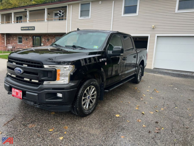 Ford F-150 police package vehicle 2020 crew cab 4x4 in black with HEA? markings on doors, front grille, red license plate, parked in lot