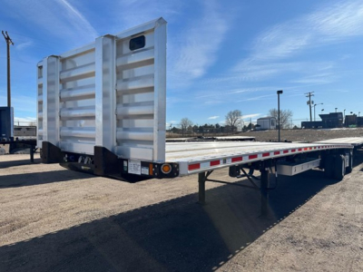 Flatbed trailer inservice with raised ramps at rear, white sides, metal deck, undercarriage and wheels visible.