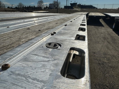 Flatbed trailer deck with metal surface, tie-down anchors, and recessed rings visible in sunlit row.