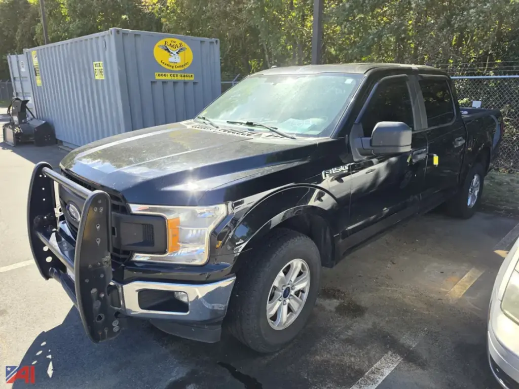 Ford F-150 pickup truck in a parking lot, black crew cab, front bumper guard installed, visible headlights and side mirror, 4x4 badge not visible.