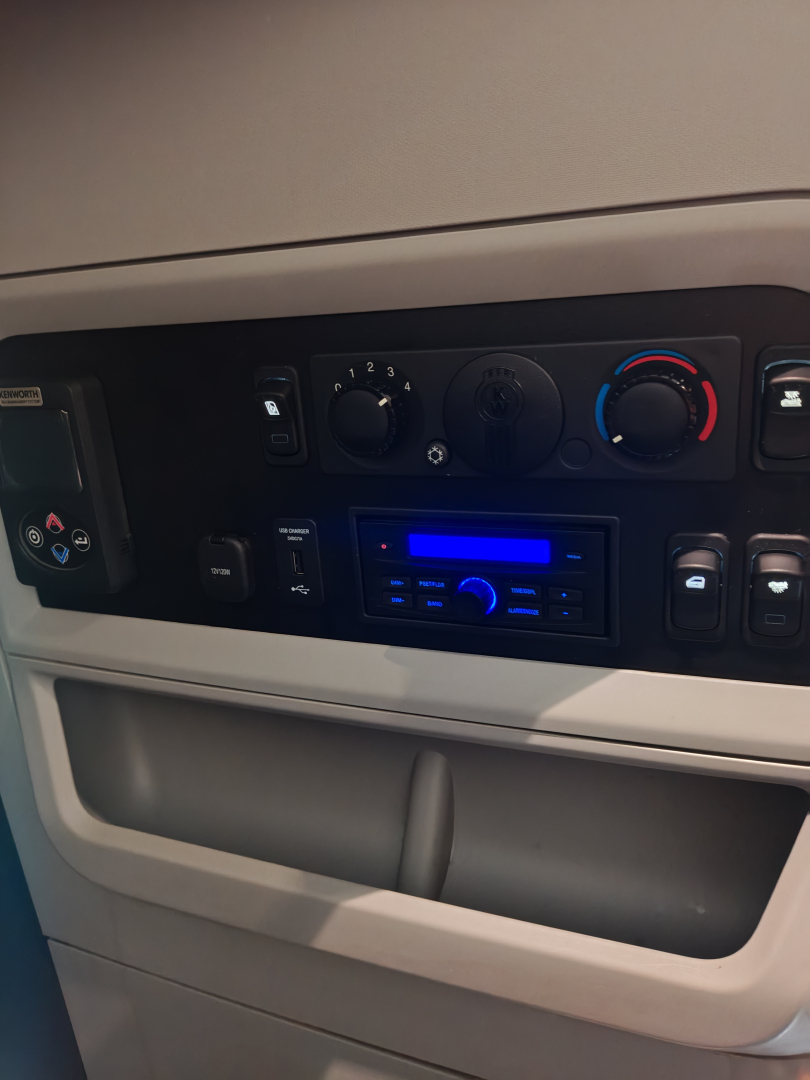 Kenworth T680 cabin dash with climate controls and radio, blue backlit display, various knobs and buttons visible.