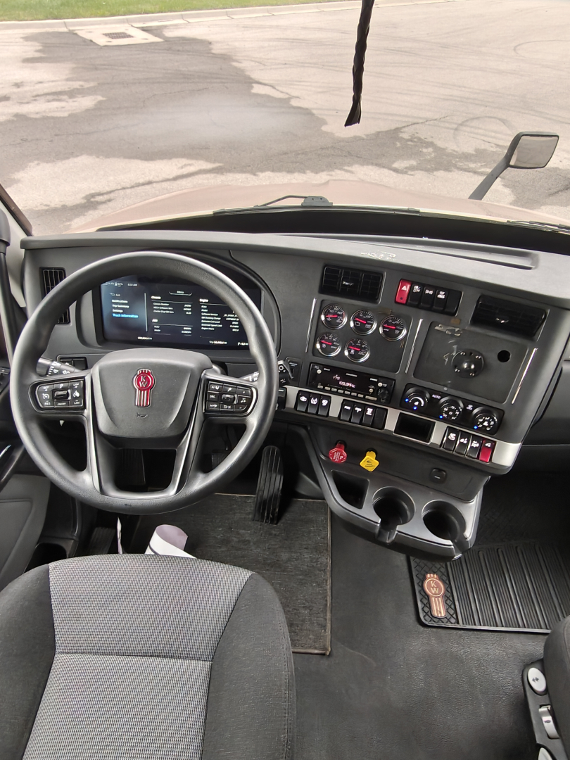 Kenworth T680 truck cab interior showing steering wheel with red logo, dashboard gauges, switches, and central console.
