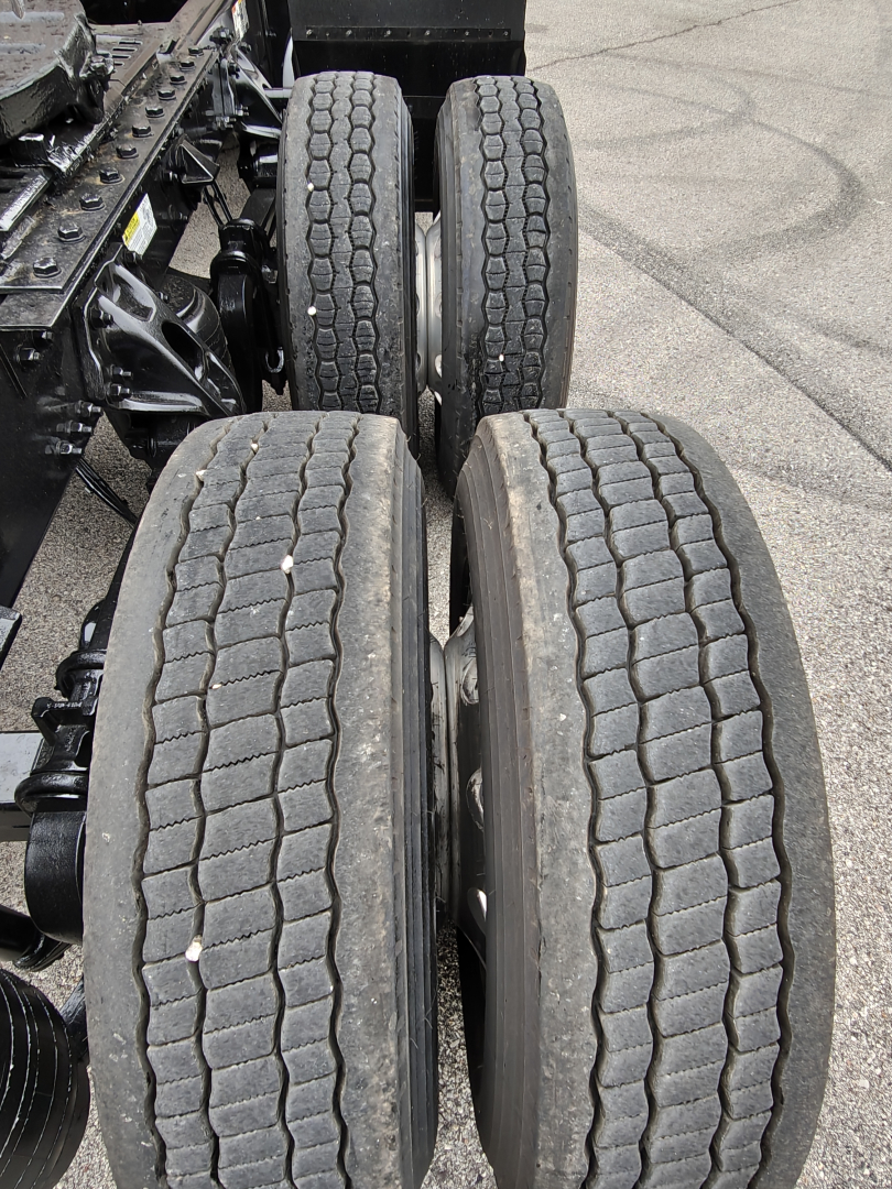 Truck chassis rear dual tandems with four wheels visible; tread pattern on tires; part of the frame and suspension; no text legible in image aside from vehicle context.