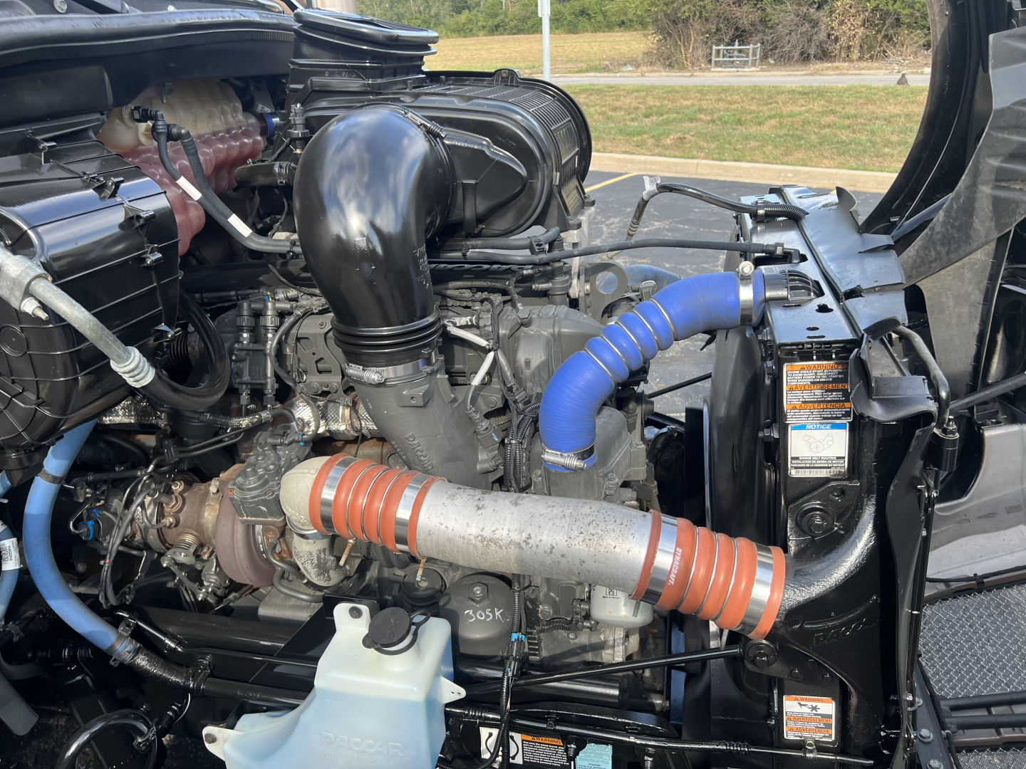 Kenworth T680 engine bay showing turbocharger, intake piping, hoses, coolant recovery bottle, and orange silicone couplers.
