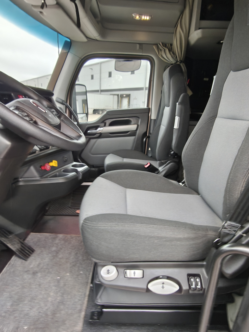 Interior cab of a Kenworth T680 truck showing driver seat and passenger seat with controls on the center console and dashboard visible.