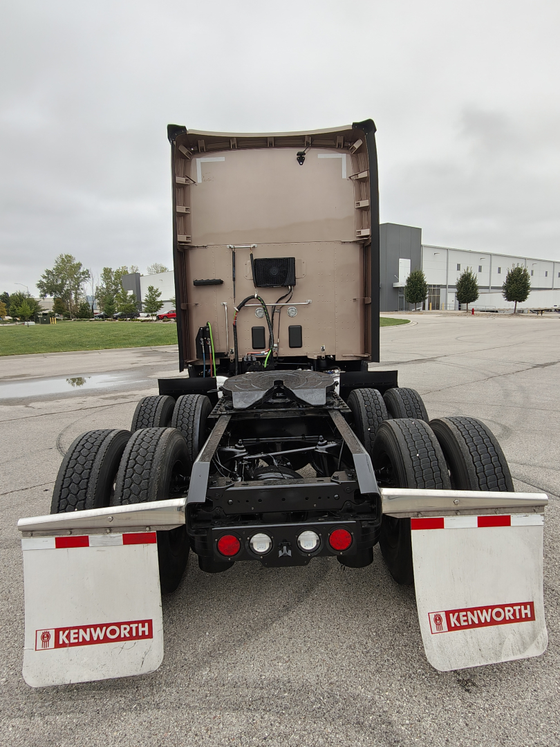 Kenworth T680 chassis rear view showing dual rear axles and Kenworth mud flaps, cab back with electrical hookups and air lines visible.