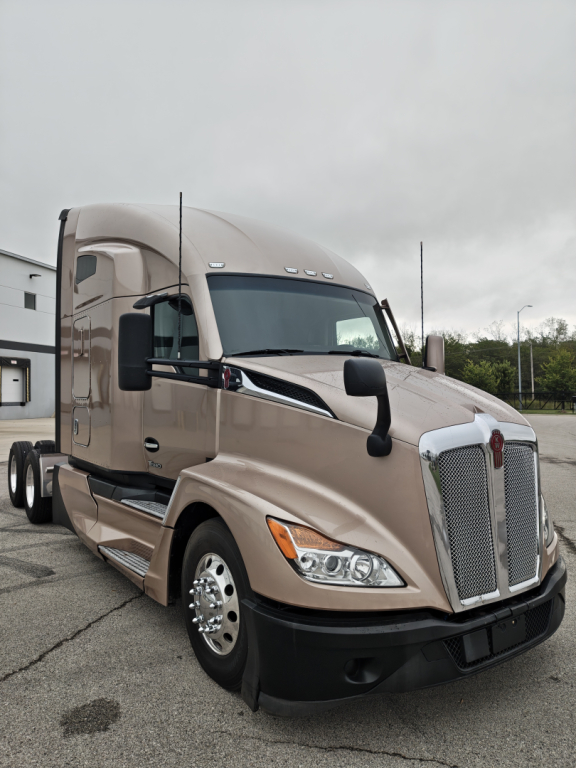 Kenworth T680 tractor; front left view; beige color; chrome grille; dual side mirrors; headlights; crew cab with aerodynamic design; wheel wells and steps visible.