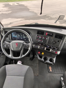 Kenworth T680 truck cab interior showing steering wheel with red logo, dashboard gauges, switches, and central console.