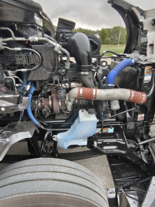 Kenworth T680 engine bay showing coolant reservoir, turbocharger, intercooler pipes, and various hoses and wiring.
