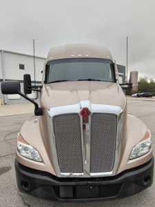 Kenworth T680 cab front view showing large chrome grille, emblem in center, beige/taupe color, prominent headlights, and black bumper.
