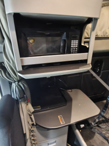 Cab interior of a Kenworth T680 showing a mounted microwave in a shelf and a folded desk/console with a control pad; no readable model text visible.