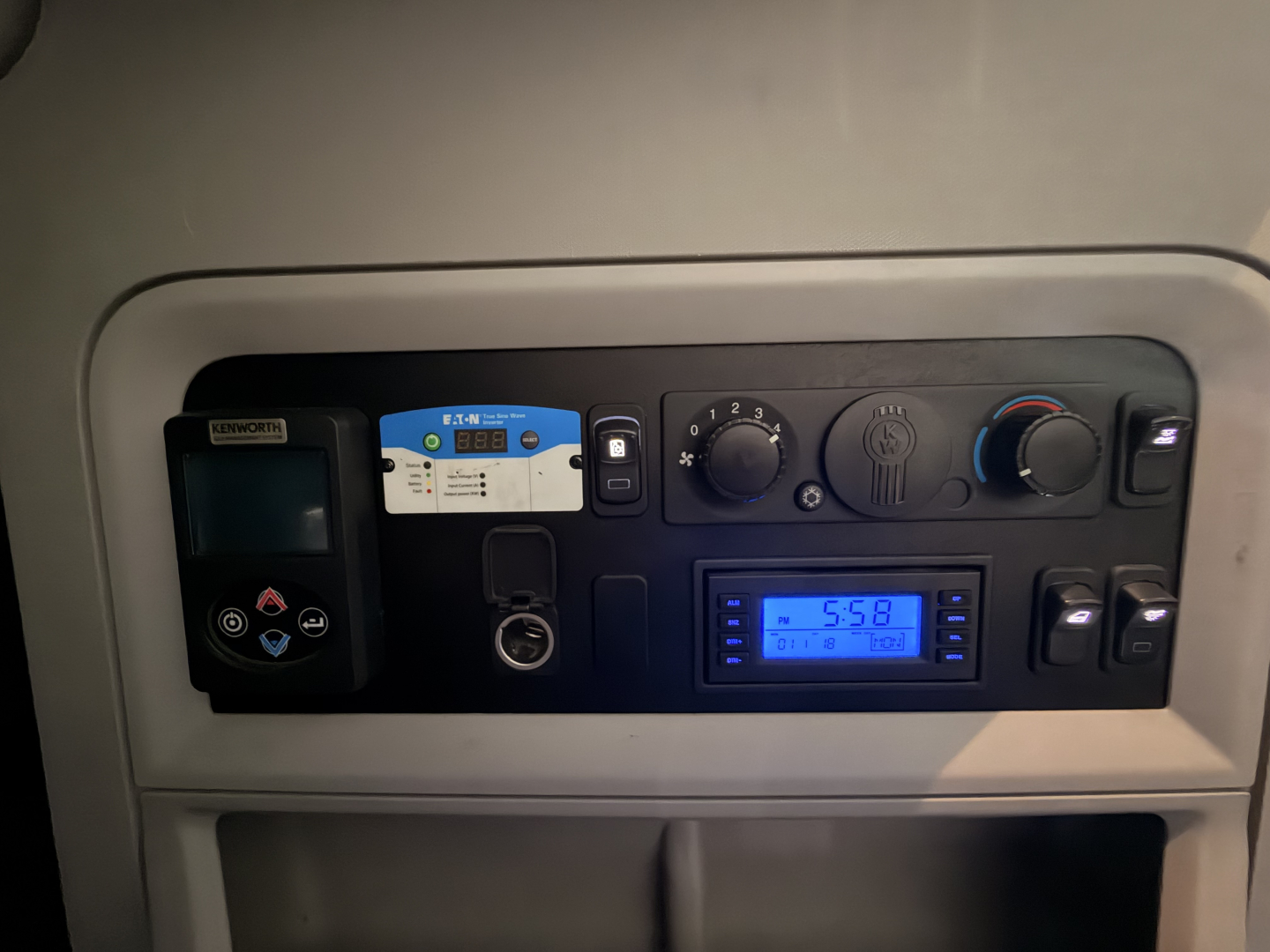 Kenworth dash panel showing digital gauge and climate controls; various switches and a card reader. Visible text includes RENWORT? and blue digital display showing 5:58.