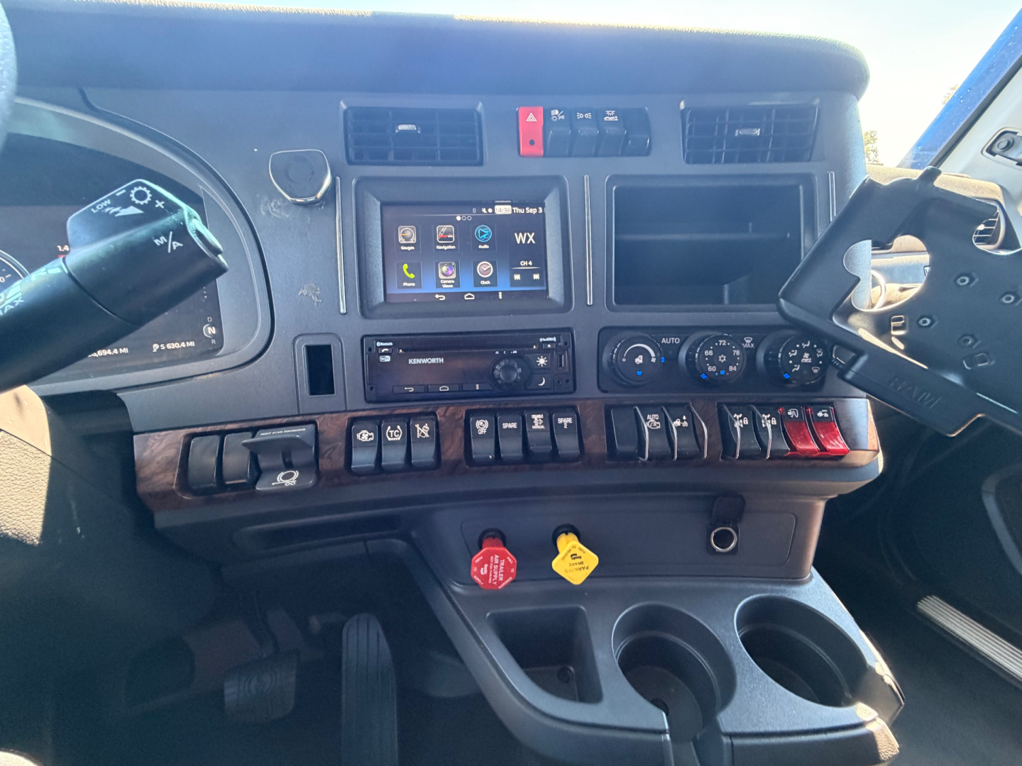 Kenworth T680 truck dashboard with steering wheels, control panel, radio screen, knobs, and switches visible.