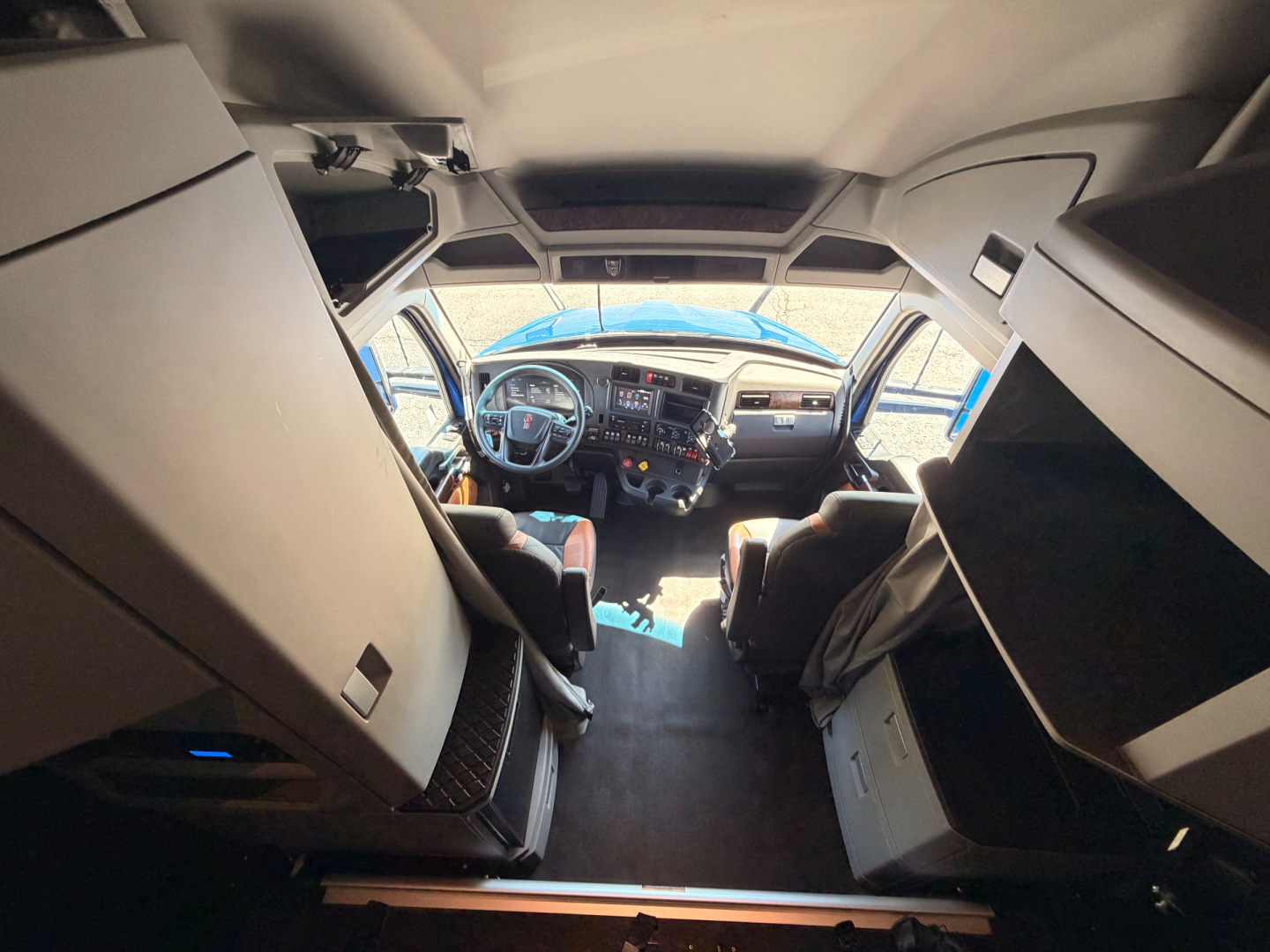 Cab interior of a Kenworth T680 truck showing driver and passenger seats, dashboard, steering wheel, and overhead storage.