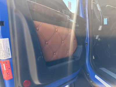 Door sill area of a blue Kenworth T680 showing tan quilted driver seat and open door
