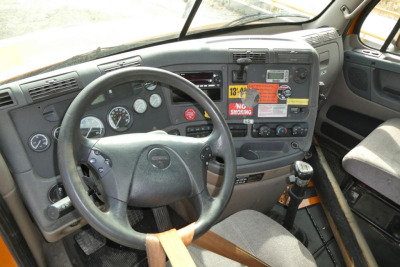 Dashboard and steering wheel of a Freightliner Cascadia 125 truck interior with gauges, controls, and label stickers visible on the dash.