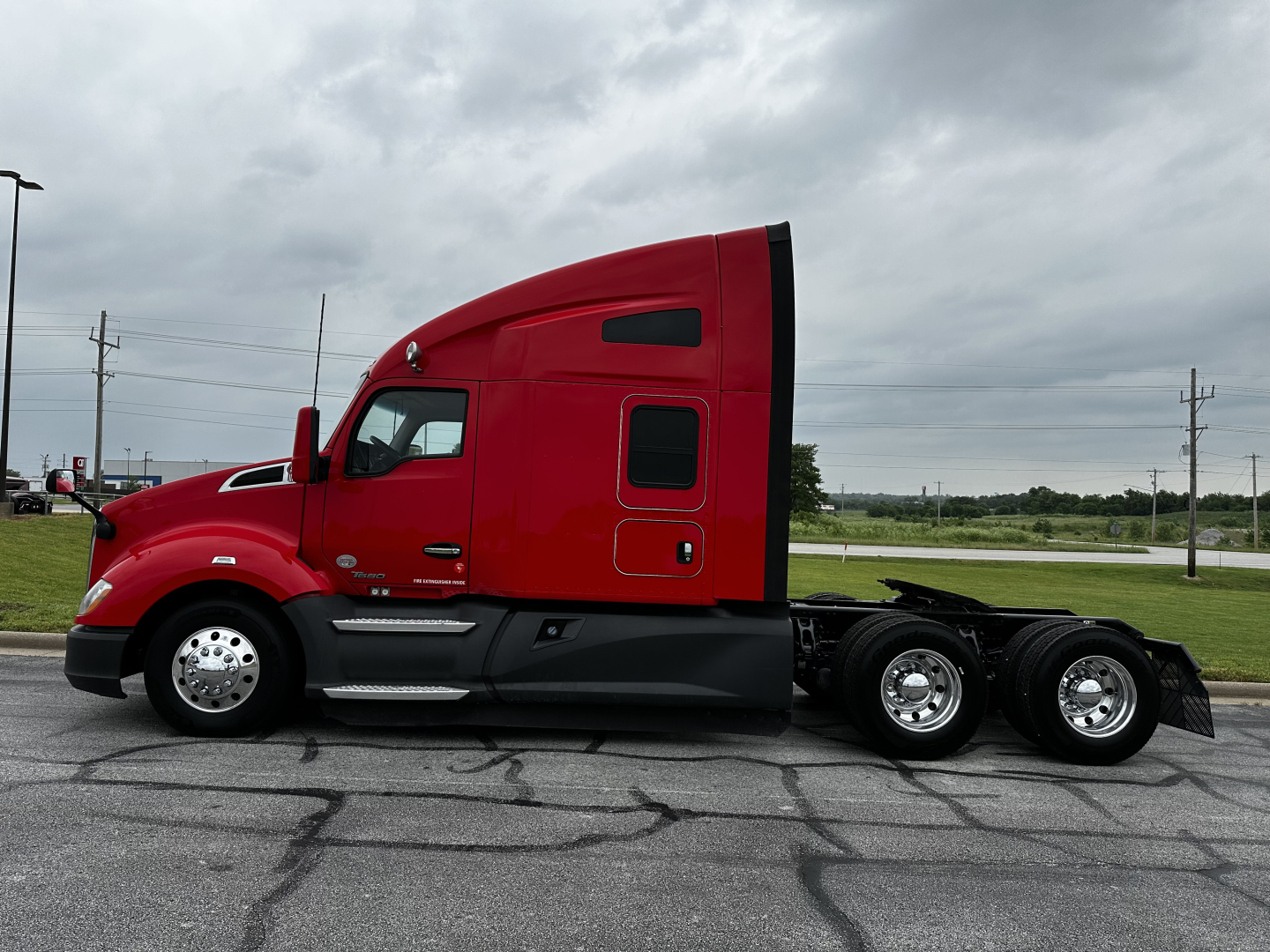 Kenworth T680 tractor in red, side view showing cab, sleeper area, chrome fuel/step rails, dual rear axles, and black chassis.
