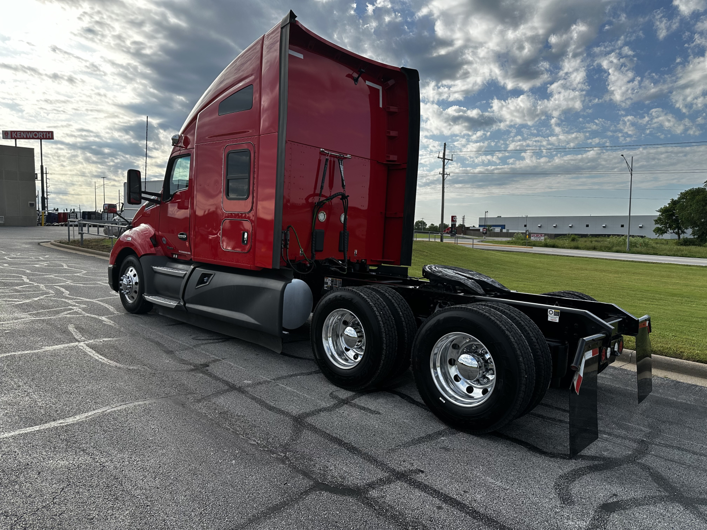 Kenworth T680 truck tractor in red, side rear view showing dual rear axles and fifth wheel, with chrome wheels and clear sky.