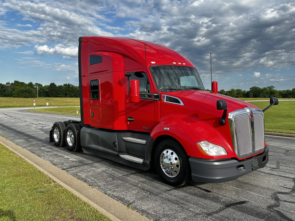 Kenworth T680 sleeper cab tractor in bright red, three-axle wheel configuration visible, chrome grille and mirrors, daytime clear sky.