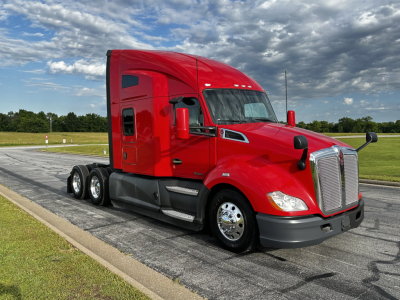 Kenworth T680 sleeper cab tractor in bright red, three-axle wheel configuration visible, chrome grille and mirrors, daytime clear sky.