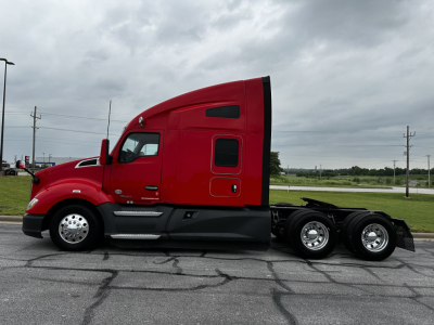 Kenworth T680 tractor in red, side view showing cab, sleeper area, chrome fuel/step rails, dual rear axles, and black chassis.