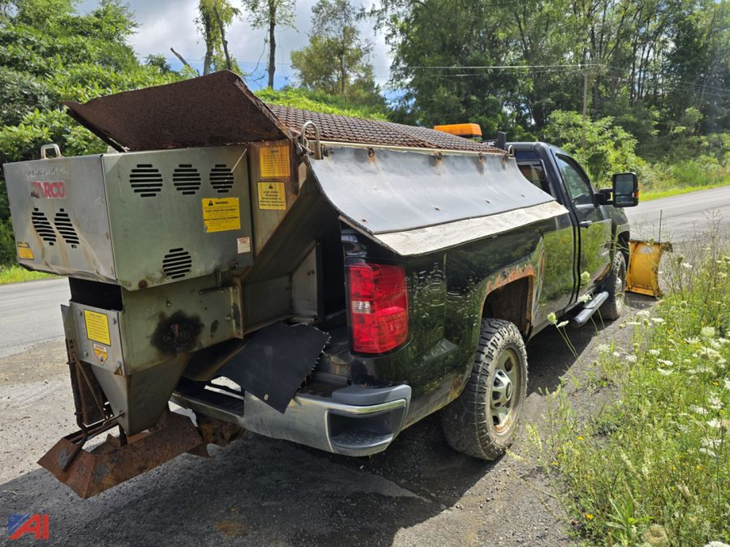 Rear/left-side view of a 2018 Chevrolet Silverado 2500HD pickup with plow and sander installed in bed, yellow hazard lights, and equipment mounted at the back.