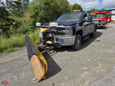 Chevrolet Silverado 2500HD pickup with snow plow and sander attachment parked on gravel; front chrome bumper, black crew cab, and yellow snow plow in foreground.