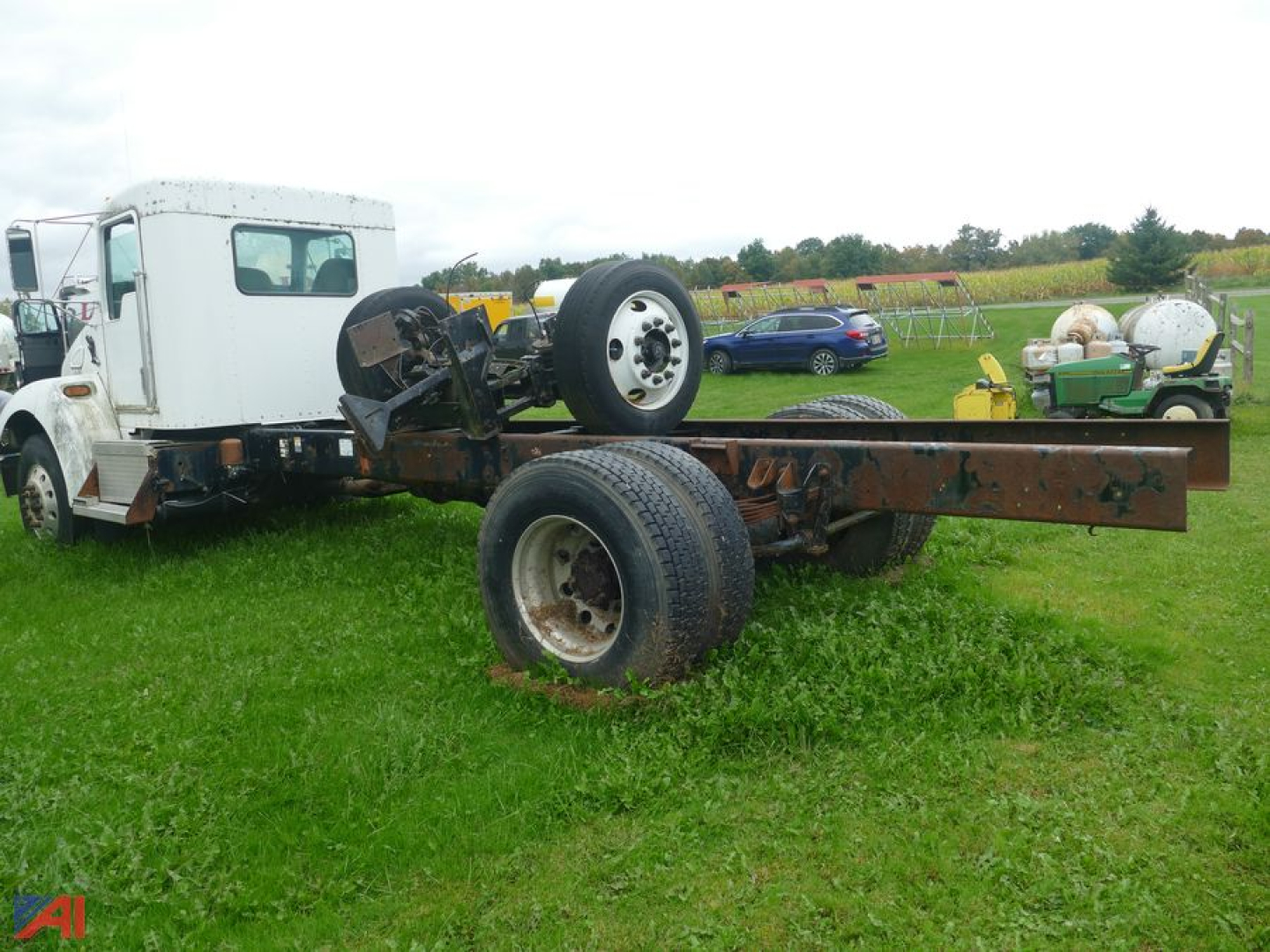 Kenworth T300 chassis cab forward view showing bare frame and rear dual wheels, front cab with a white exterior, overcast field in background.