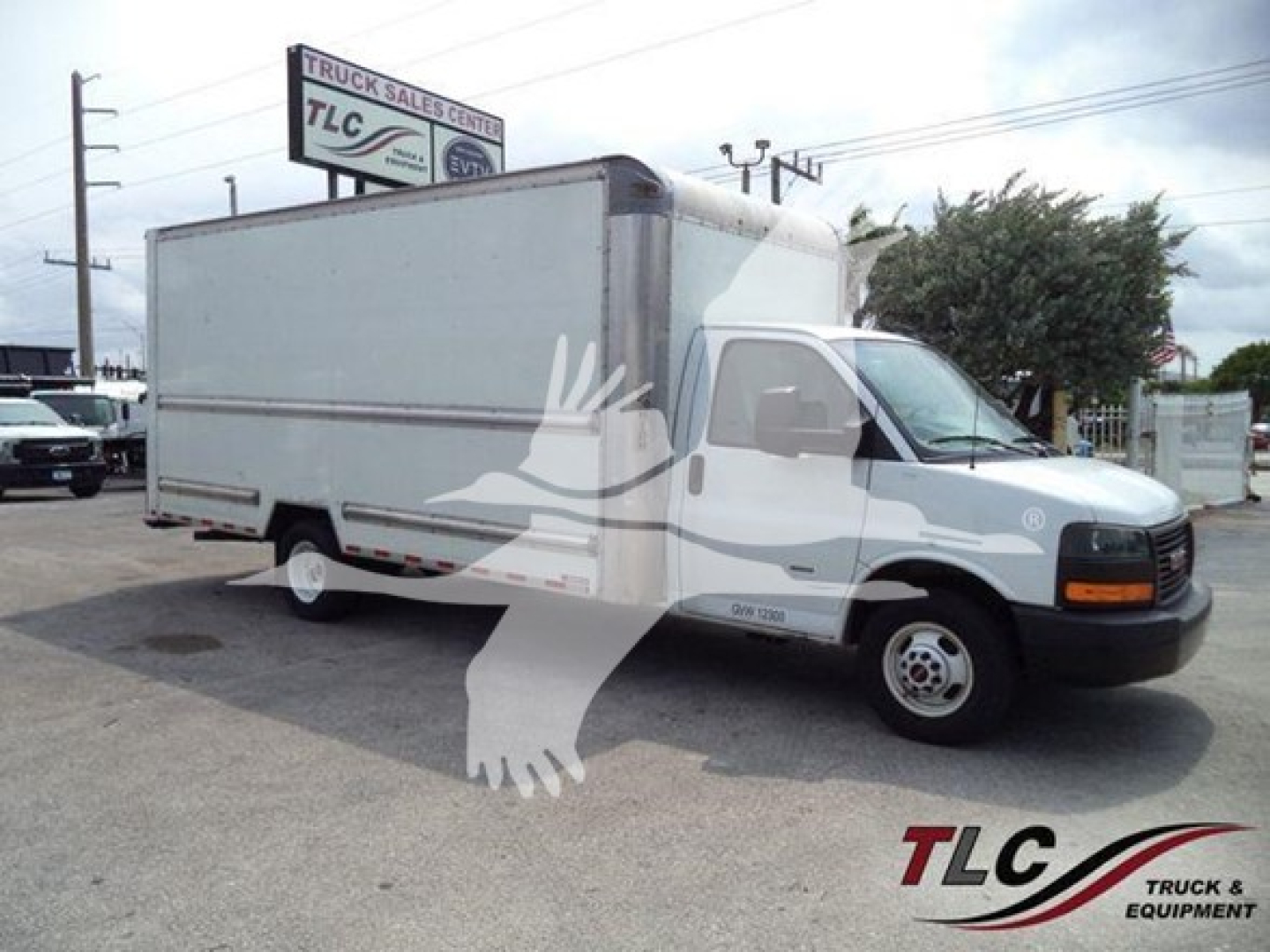 Box truck on lot with GMC G3500 cab in foreground, TLG Truck Sales Center sign, stock number T10245 and VIN on image.