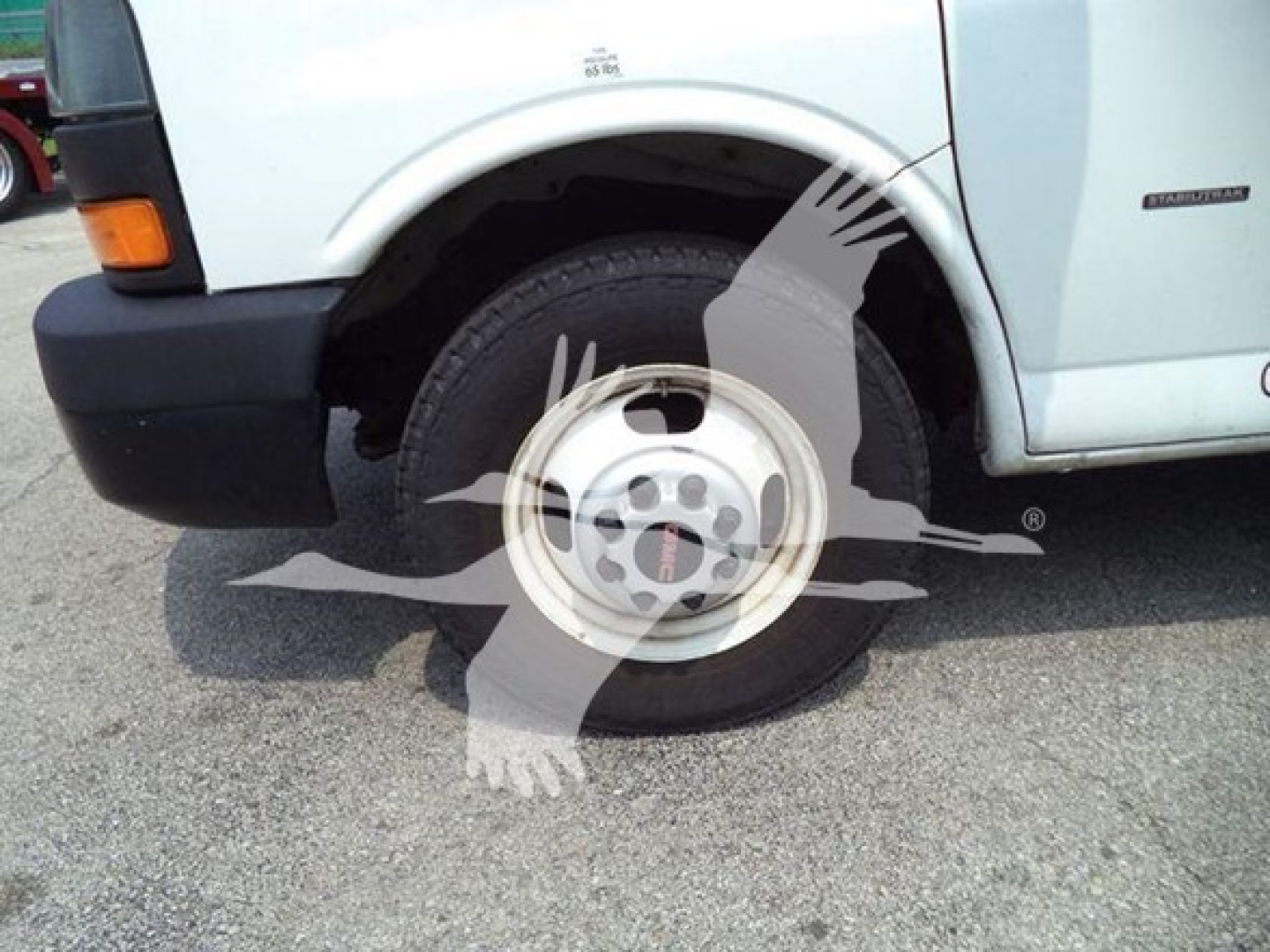 Front-left wheel and fender of a light-duty GMC G3500 cargo van showing wheel, tire, and side badge in a parking lot.