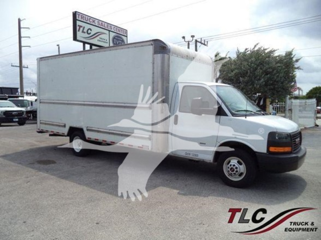 Box truck on lot with GMC G3500 cab in foreground, TLG Truck Sales Center sign, stock number T10245 and VIN on image.