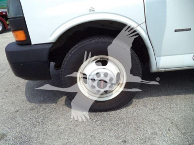 Front-left wheel and fender of a light-duty GMC G3500 cargo van showing wheel, tire, and side badge in a parking lot.