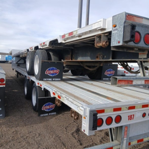 Manac combo drop deck trailer on a stacked transport with dual rear axles and reflective safety tape, Utility Wyoming mud flaps, and rear lights visible.