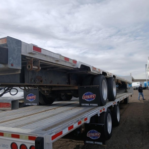 Manac combo drop deck trailer on a flatbed with multiple axles and wheels visible, Utility banners on mudflaps, in-service condition.