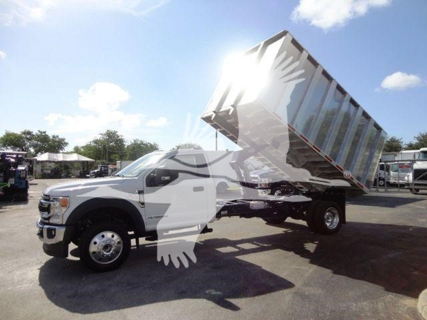 Dump truck with raised dump bed on a Ford F-550 chassis, front wheel and cab visible, yard setting in background.
