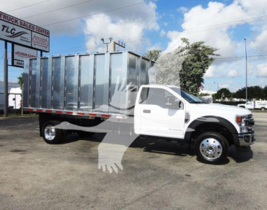 Ford F-550 dump truck in a dealership lot with a large metal dump bed and white cab, STOCK number F5504X4CHIPPER visible in listing