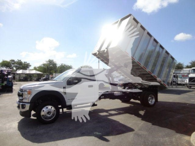 Dump truck with raised dump bed on a Ford F-550 chassis, front wheel and cab visible, yard setting in background.