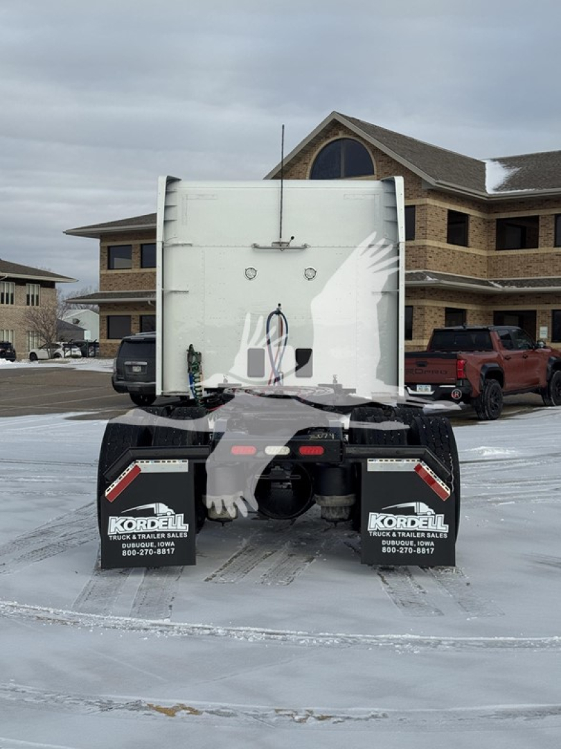 Rear view of a 2019 Peterbilt 579 truck with a white truck bed and mud flaps, parked on a snowy lot in front of a building.
