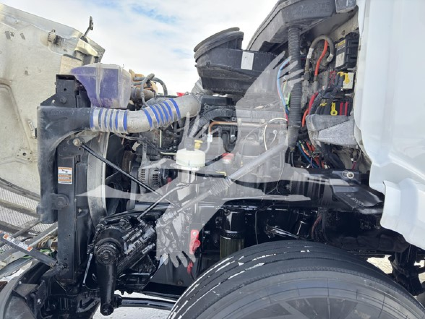 Peterbilt 579 engine bay and front chassis showing radiator, hoses, wiring, and steering area with exposed engine components.